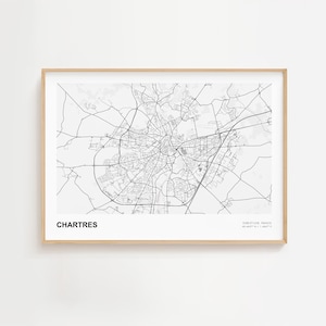 May include: A framed black and white map print of Chartres, France. The map shows the city's road network and is labeled with the city name at the bottom left and coordinates at the bottom right. The frame is a light wood color.