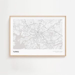 Op de afbeelding: Een ingelijste kaartafdruk van Turku, Finland, in zwart en wit. De kaart toont het wegennetwerk van de stad en de omgeving. Het woord "TURKU" staat in het zwart linksonder. De lijst heeft een lichte houtkleur.