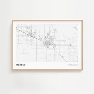 May include: A framed black and white map print of Merced, California, with the city name printed in bold letters at the bottom left. The map shows the city's layout, streets, and surrounding areas. The frame is a light wood color.