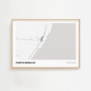 May include: A framed print showing a minimalist black and white map of Puerto Morelos, Mexico. The town's name is at the bottom. The frame is light wood, and the print is set against a white background.