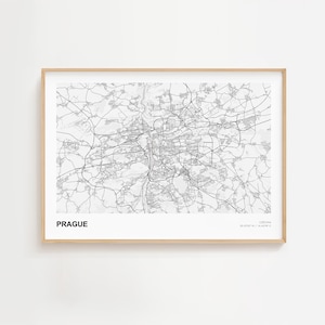 Op de afbeelding: Een ingelijste zwart-wit kaart van Praag, Tsjechië. De kaart toont het wegennetwerk en het riviersysteem van de stad. Het woord "PRAGUE" staat vetgedrukt in zwarte letters linksonder. De lijst is gemaakt van lichtgekleurd hout.