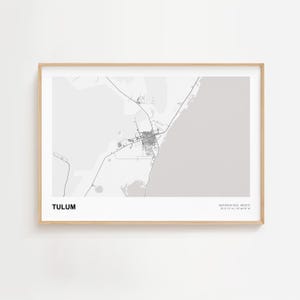 Puede incluir: Una impresión enmarcada de un mapa de Tulum, México, en escala de grises. El mapa muestra el diseño de la ciudad con carreteras y edificios. El texto "TULUM" está en la parte inferior izquierda, con coordenadas en la inferior derecha. El marco es de madera clara.