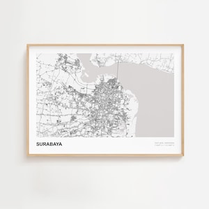 May include: A framed black and white map print of Surabaya, East Java, Indonesia. The map shows the city's layout with roads, buildings, and waterways. The city name is printed in a bold font at the bottom left.