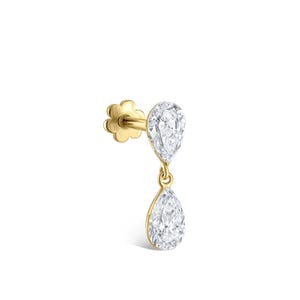 Puede incluir: Un pendiente de oro con dos piedras preciosas claras en forma de pera. La piedra superior es fija, mientras que la inferior cuelga. El pendiente tiene un respaldo en forma de flor.