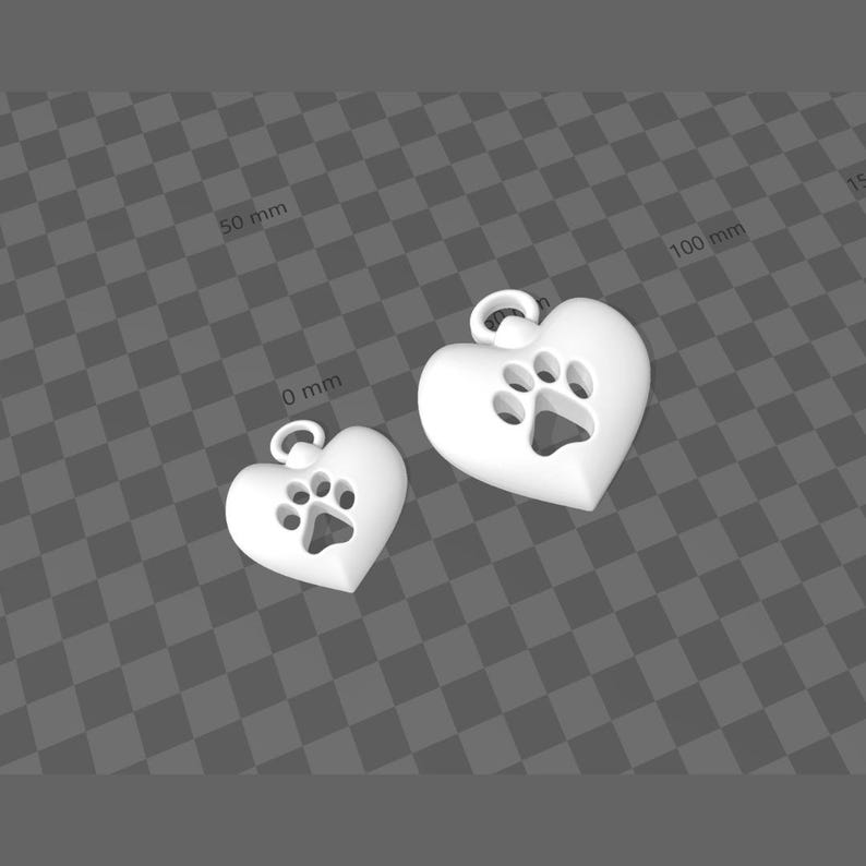 Puede incluir: Dos colgantes blancos en forma de coraz&oacute;n con un dise&ntilde;o de huella recortada y un peque&ntilde;o lazo circular en la parte superior para su fijaci&oacute;n. Los colgantes se muestran sobre un fondo de cuadr&iacute;cula con medidas m&eacute;tricas visibles en mil&iacute;metros.