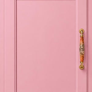 Könnte beinhalten: Eine rechteckige Schranktür in mattem Rosa mit einem erhabenen Rahmen. An der rechten Seite befindet sich ein vertikaler Griff mit einem dekorativen orange-schwarzen Muster in der Mitte und Endstücken aus poliertem, goldfarbenem Metall.