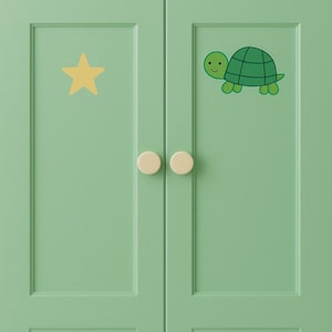 Op de afbeelding: Een lichtgroene kast met een gele ster en een groene schildpadillustratie. De kast heeft twee ronde, crèmekleurige knoppen. De schildpad heeft een groen schild en een lachend gezicht.