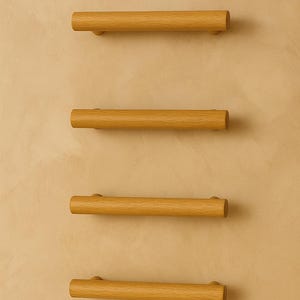 May include: Four wooden cabinet pulls with a cylindrical design. The pulls are made of light-colored wood and are mounted on a beige wall. The pulls are evenly spaced and horizontally aligned, offering a minimalist aesthetic.