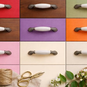 Puede incluir: Una colección de tiradores de armario con asas de cerámica blanca y extremos metálicos ornamentados de estilo antiguo. Los tiradores se muestran sobre una variedad de fondos coloridos, incluyendo rojo, marrón, morado y naranja. Herrajes decorativos para muebles.