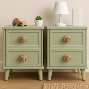 Puede incluir: Dos mesitas de noche verde salvia con dos cajones cada una, con tiradores de nudo de cuerda. Una lámpara blanca, una pequeña suculenta y una caja de lunares están encima de una. Un coche de juguete de madera está en la otra.