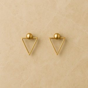 以下が含まれることがあります： 2つの金色のキャビネットノブ。各ノブは、上部に小さな球が付いた三角形の形状をしています。ノブは、ニュートラルな明るい色の背景に対して設定されています。