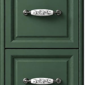 May include: A close-up of a green cabinet with two drawers. Each drawer features a decorative white and black porcelain handle with a floral design. The handles are mounted on a dark metal base.