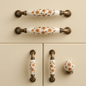 May include: A selection of cabinet hardware with floral patterns. The image displays two long, oval handles and two smaller pull handles, plus a round knob. The hardware has a white base with orange and green floral designs and bronze-coloured metal accents.