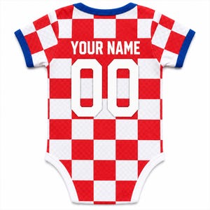 K&ouml;nnte beinhalten: Ein kurz&auml;rmeliger Baby-Body mit rot-wei&szlig;em Karomuster. Auf der R&uuml;ckseite befindet sich der Text YOUR NAME in wei&szlig;en Gro&szlig;buchstaben &uuml;ber der gro&szlig;en wei&szlig;en Zahl 00. Das Kleidungsst&uuml;ck hat blaue Einfassungen am Halsausschnitt und an den &Auml;rmeln.