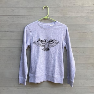 May include: A gray sweatshirt with a black and white graphic of an eagle flying with a crescent moon and trees in the background.