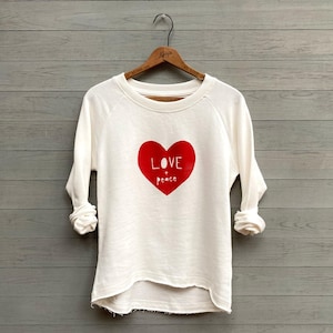 May include: White sweatshirt with a red heart graphic that says "LOVE & peace" on it.