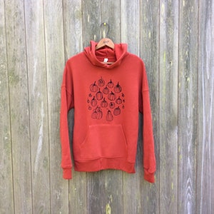May include: A rust-colored hoodie with a black print of a circle of pumpkins. The hoodie has a drawstring hood and a kangaroo pocket.