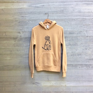 May include: A tan hoodie with a black outline of a dog on the front. The hoodie has a hood and a kangaroo pocket.