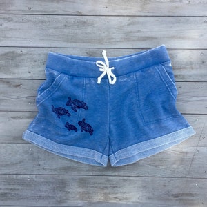 Peut inclure: Short en jean bleu avec un cordon de serrage blanc et un motif de cinq tortues de mer en cercle.