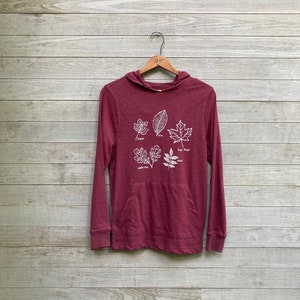 May include: A maroon long-sleeved hoodie with a pocket and a white graphic of five different leaves with their names: Poplar, Elm, Sugar Maple, White Oak, and Ash.