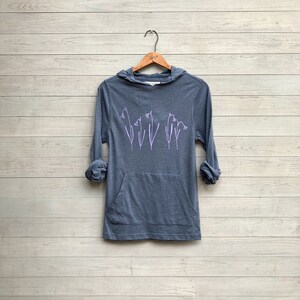 Puede incluir: Una sudadera con capucha azul oscuro con un bolsillo y un diseño floral morado en la parte delantera.