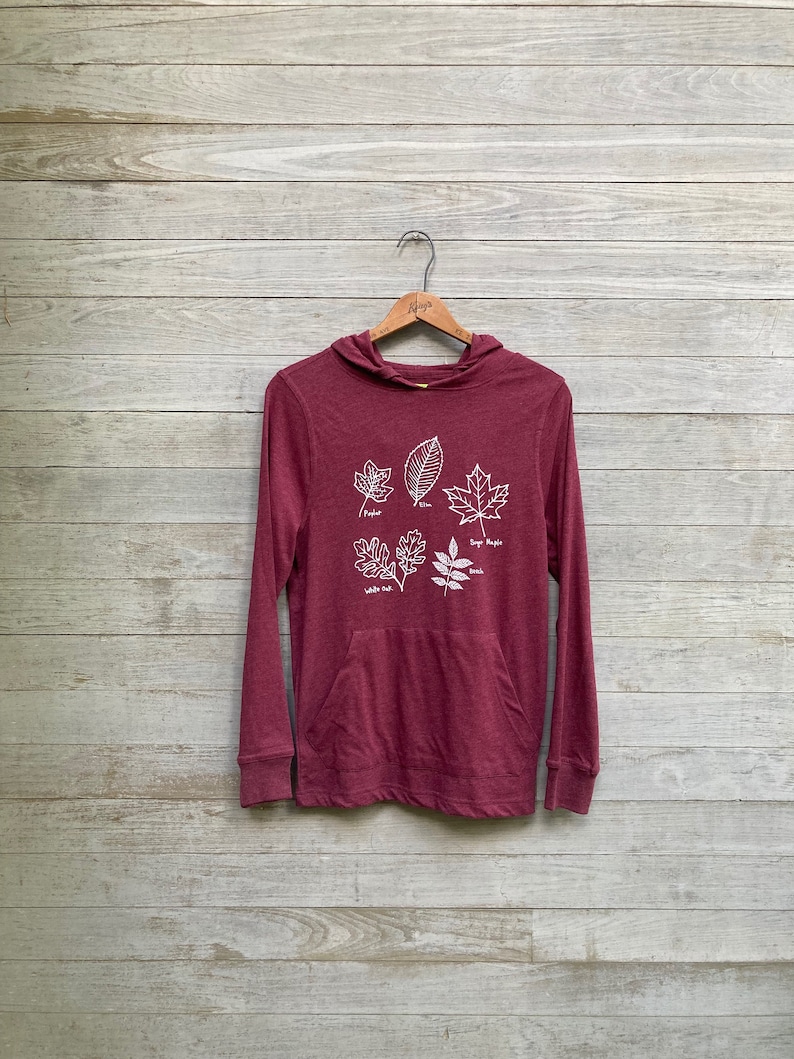 May include: A maroon long-sleeved hoodie with a pocket and a white graphic of five different leaves with their names: Poplar, Elm, Sugar Maple, White Oak, and Ash.