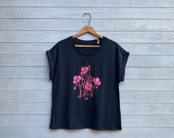 Puede incluir: Camiseta negra con estampado floral rosa de amapolas. La camiseta tiene mangas cortas y un corte holgado.