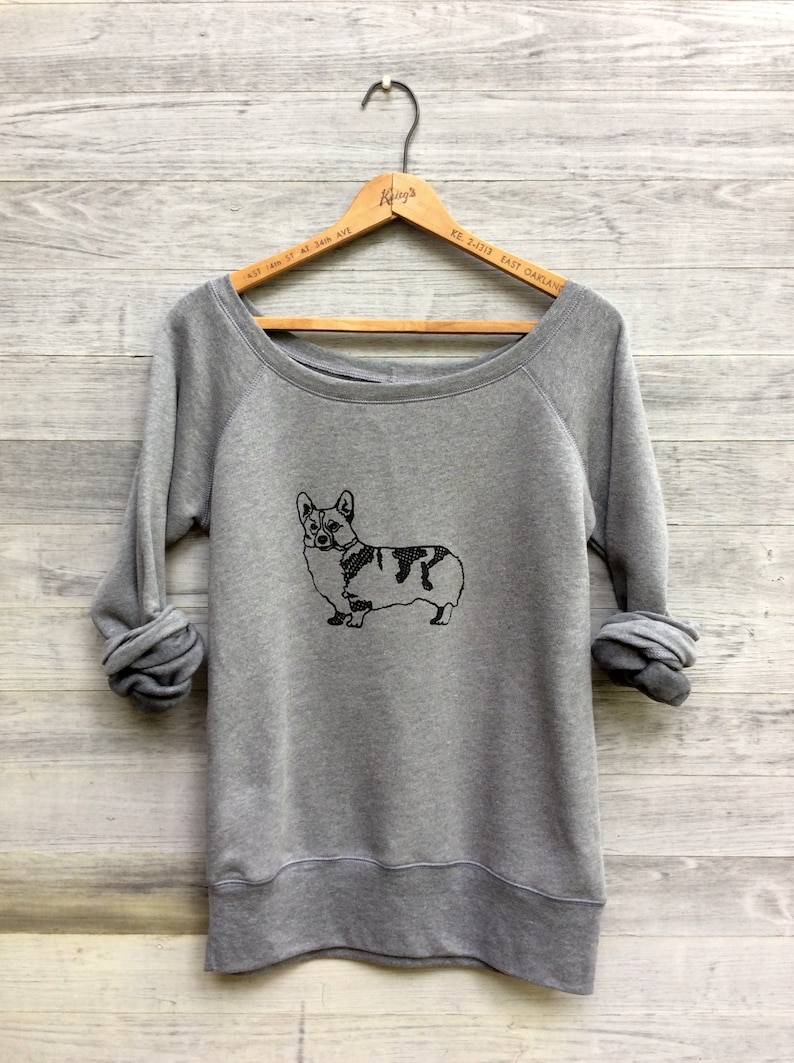 May include: Gray sweatshirt with a black and white outline of a corgi dog on the front. The sweatshirt has a wide neckline and long sleeves.