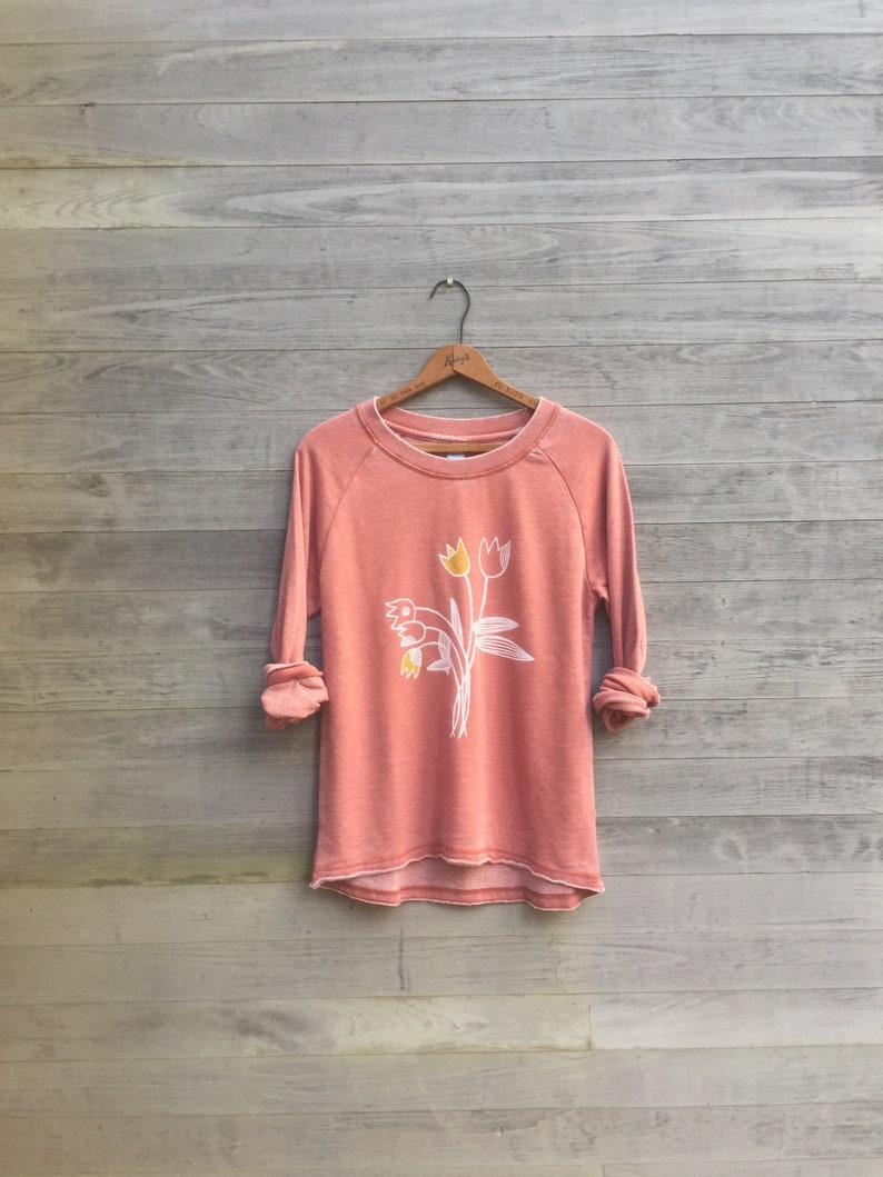 May include: A coral colored sweatshirt with a white graphic of a bouquet of tulips with yellow centers.