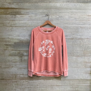 May include: A coral-colored sweatshirt with a white floral design. The sweatshirt has long sleeves and a relaxed fit.