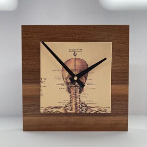 May include: A wooden clock with a skeletal image on the face. The clock hands are black and the clock face is a vintage anatomical illustration of a human skeleton.