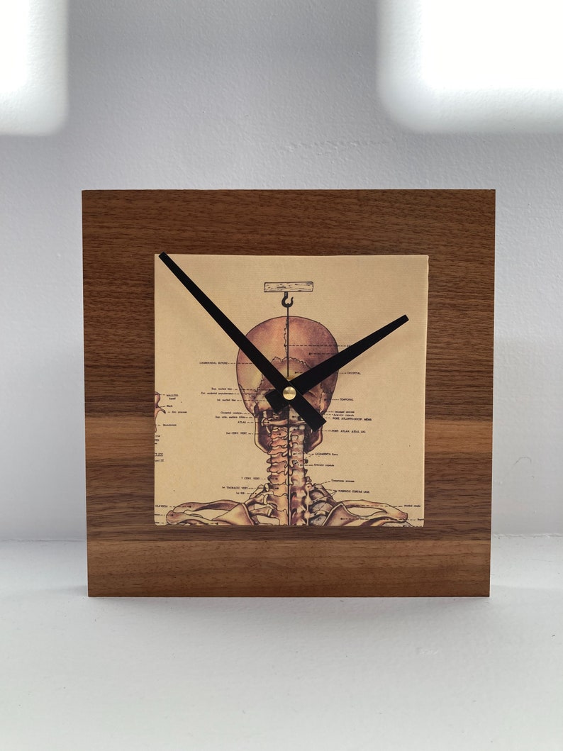 May include: A wooden clock with a skeletal image on the face. The clock hands are black and the clock face is a vintage anatomical illustration of a human skeleton.