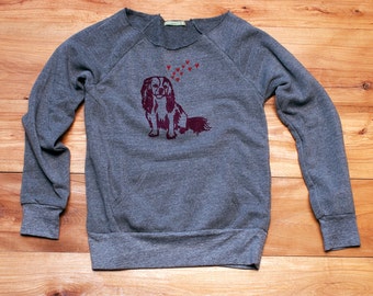 May include: Gray sweatshirt with a graphic of a Cavalier King Charles Spaniel with hearts above its head.