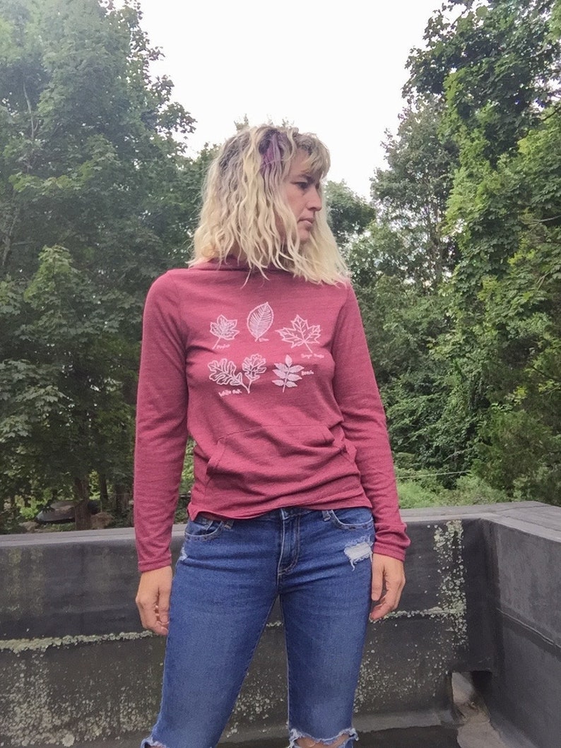 May include: A maroon long-sleeved hooded sweatshirt with a white graphic of five different leaves. The leaves are labeled with their names: "Sugar Maple", "White Oak", "Red Oak", "Willow Oak", and "Sassafras".