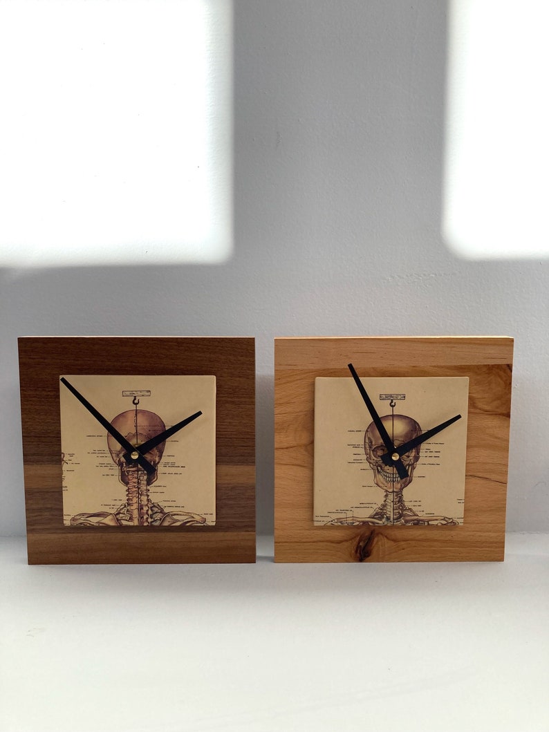 May include: Two wooden clock bases with a skeleton clock face featuring a skull and spine. The clock faces are printed with anatomical illustrations.