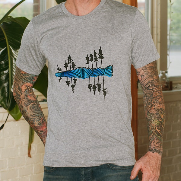 May include: A gray t-shirt with a graphic of a forest reflected in a lake. The graphic is made up of black trees and a blue and white patterned lake.