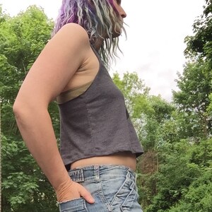 May include: A gray cropped tank top with a scoop neck and a relaxed fit. The tank top is worn with blue denim jeans.