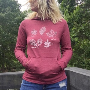 May include: A maroon hoodie with a white outline of five different leaves. The leaves are labeled with their names: "Pepper", "Elm", "Sugar Maple", "White Oak", and "Ash".