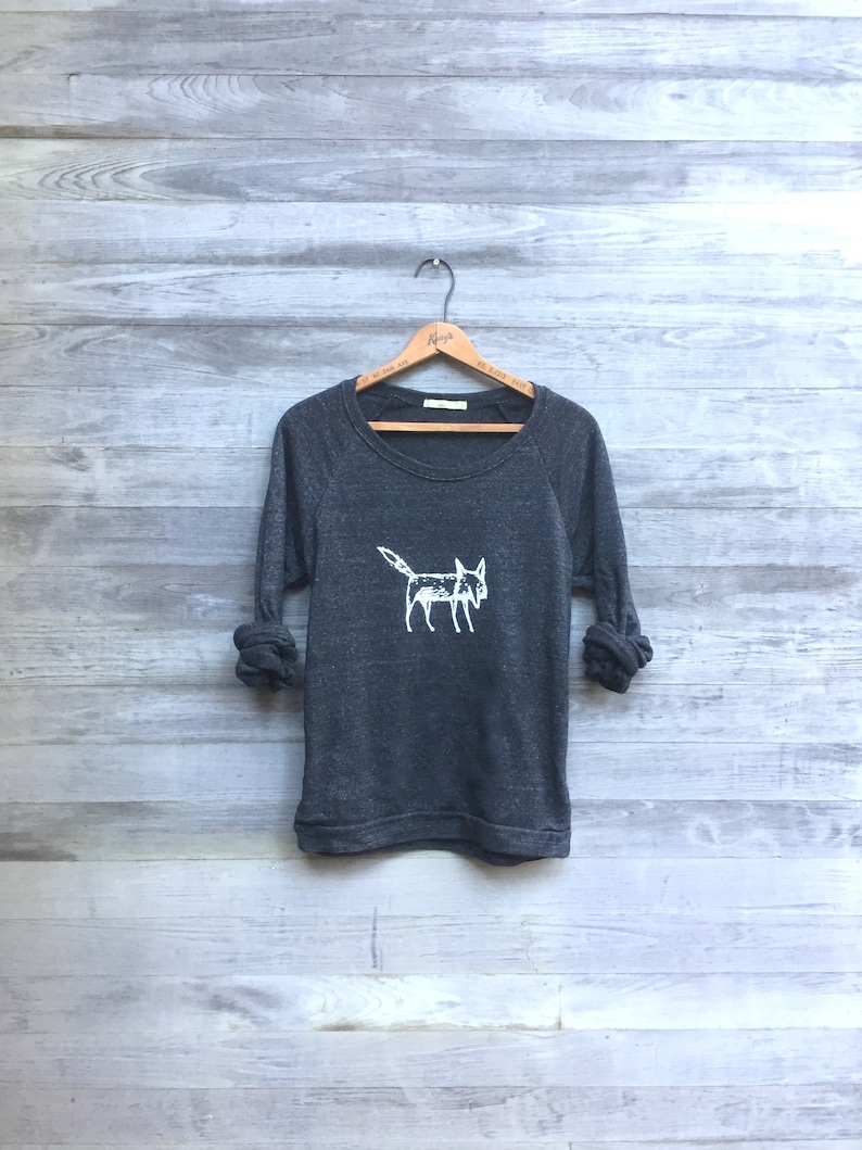 May include: A dark gray sweatshirt with a white fox graphic on the front. The sweatshirt has a crew neck and long sleeves.