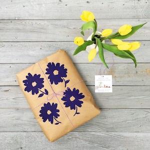 May include: A brown paper gift bag with a purple floral design and a white gift tag that says "Nicola + The Newfoundlanders".