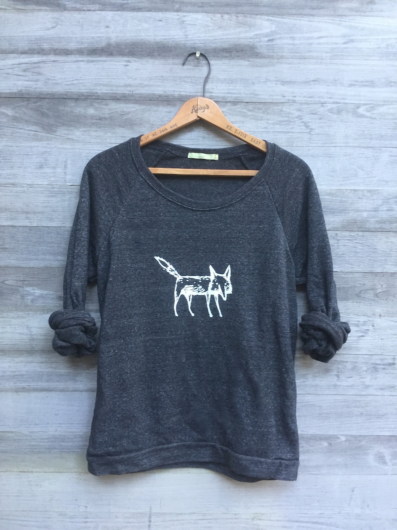 May include: A dark gray sweatshirt with a white graphic of a fox on the front. The sweatshirt has long sleeves and a crew neck.