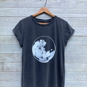 K&ouml;nnte beinhalten: Ein dunkelgraues T-Shirt mit einem wei&szlig;en Mondmotiv auf der Vorderseite.