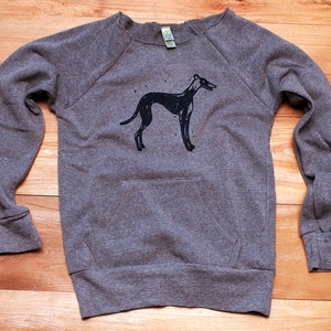 May include: A gray sweatshirt with a black silhouette of a dog on the front. The sweatshirt has a crew neck and long sleeves.