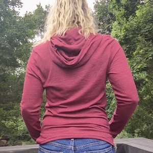 May include: A maroon long-sleeved hooded shirt with a fitted silhouette. The shirt is made of a soft, comfortable fabric and has a relaxed, casual look.