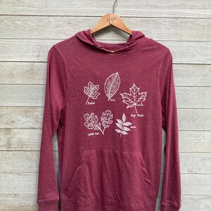 May include: Burgundy long-sleeve hooded sweatshirt with a white graphic of five different types of leaves with their names: Poplar, Elm, Sugar Maple, White Oak, and Beech.