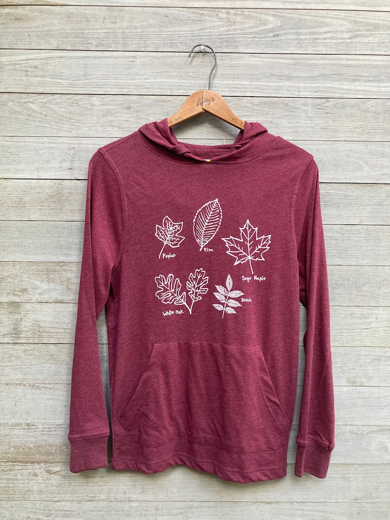 May include: Burgundy long-sleeve hooded sweatshirt with a white graphic of five different types of leaves with their names: Poplar, Elm, Sugar Maple, White Oak, and Beech.