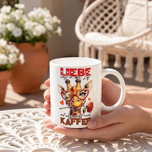 Könnte beinhalten: Weiße Keramik-Tasse mit einem Giraffen-Design, die eine herzförmige Brille trägt und eine rote Rose hält. Mit deutschem Text: "LIEBE liegt in der Luft" und "und sie sehnt nach KAFFEE."