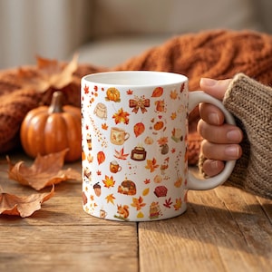 Könnte beinhalten: Ein weißer Keramikbecher mit einem sich wiederholenden Muster aus herbstlichen Illustrationen, darunter orangefarbene Kürbisse, rote und gelbe Ahornblätter, braune Eichhörnchen, Pullover, Heißgetränke, Eicheln und kleine Igel auf einer glatten Oberfläche.