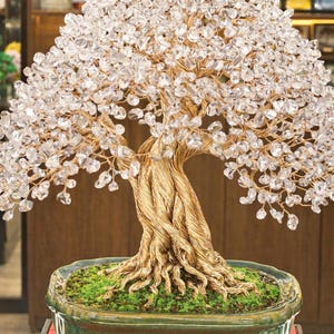 May include: A handcrafted bonsai tree sculpture with a textured, golden-colored trunk and branches. The tree's foliage is composed of clear, sparkling crystals. The bonsai sits in a green ceramic pot with a mossy base, creating a unique decorative piece.