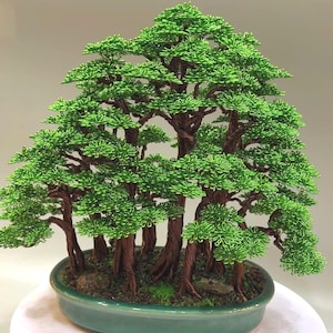 May include: A handcrafted bonsai tree sculpture. The miniature tree features a cluster of brown wire trunks supporting vibrant green wire foliage. The bonsai is planted in a teal oval ceramic pot, creating a serene and natural aesthetic.